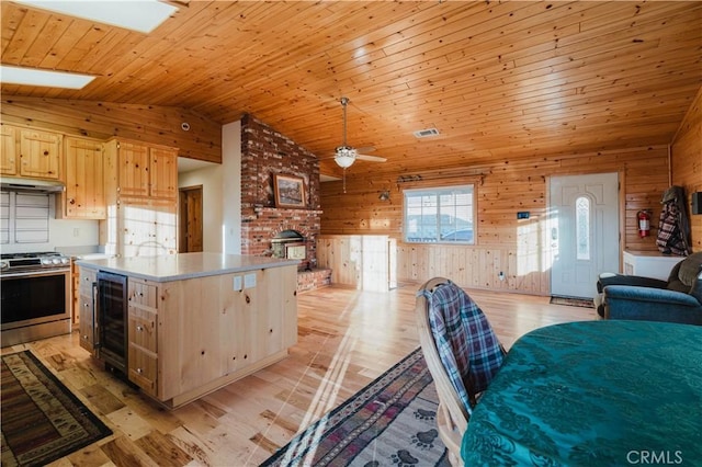 kitchen featuring ceiling fan, stainless steel gas range oven, light brown cabinetry, lofted ceiling with skylight, and wood ceiling