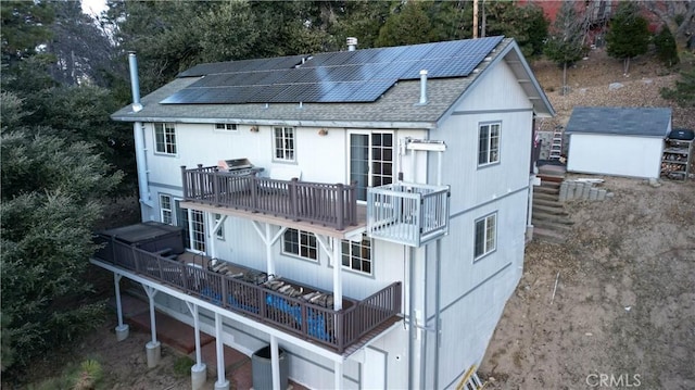 rear view of property with a balcony, a wooden deck, a storage shed, and solar panels