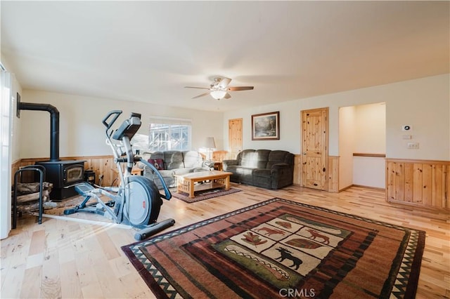 living room featuring ceiling fan, wood walls, a wood stove, and wood-type flooring