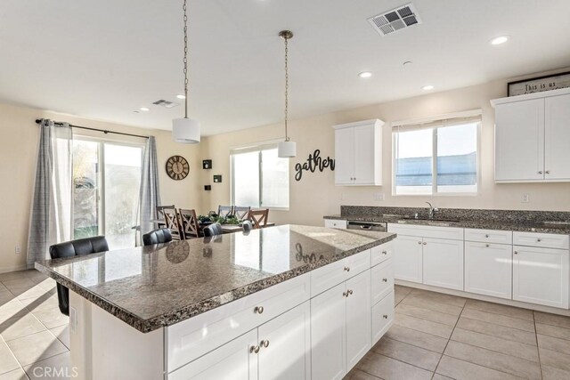 kitchen with light tile patterned floors, pendant lighting, a kitchen island, sink, and white cabinetry