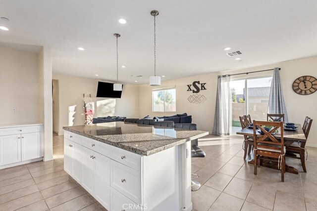 kitchen with a breakfast bar area, hanging light fixtures, dark stone counters, a kitchen island, and white cabinets