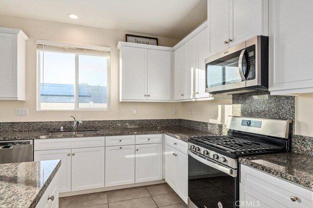 kitchen featuring sink, white cabinets, dark stone countertops, light tile patterned floors, and appliances with stainless steel finishes