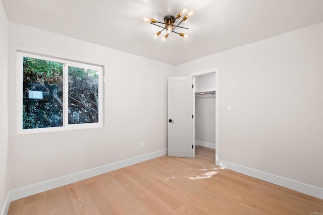 unfurnished bedroom with a closet, light wood-type flooring, and a notable chandelier