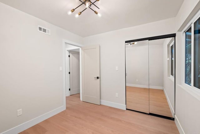 unfurnished bedroom featuring a closet, light wood-type flooring, and a notable chandelier