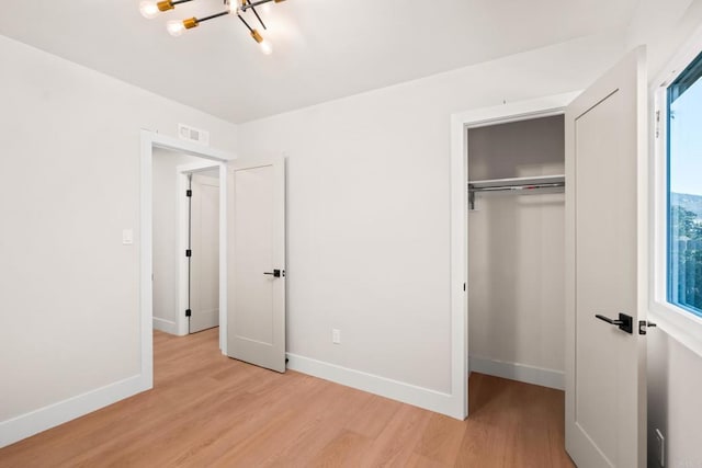 unfurnished bedroom with a closet, an inviting chandelier, and light hardwood / wood-style flooring