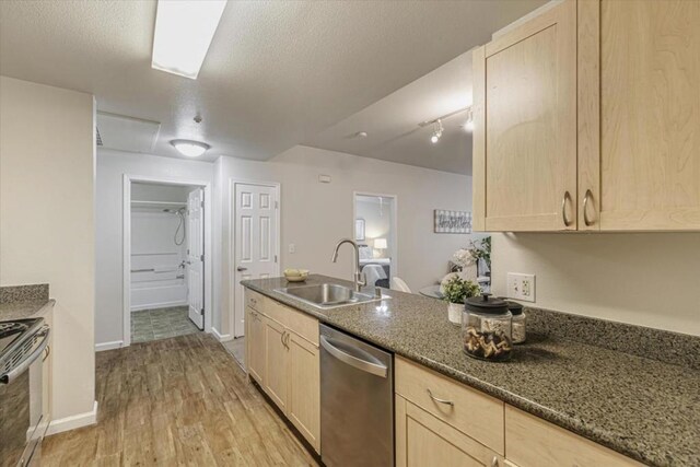 kitchen featuring sink, light brown cabinets, dark stone countertops, light hardwood / wood-style floors, and appliances with stainless steel finishes