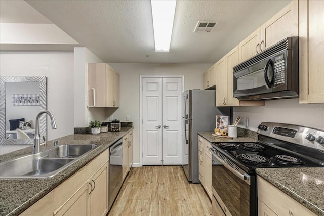 kitchen with stainless steel appliances, sink, a textured ceiling, light brown cabinets, and light hardwood / wood-style floors