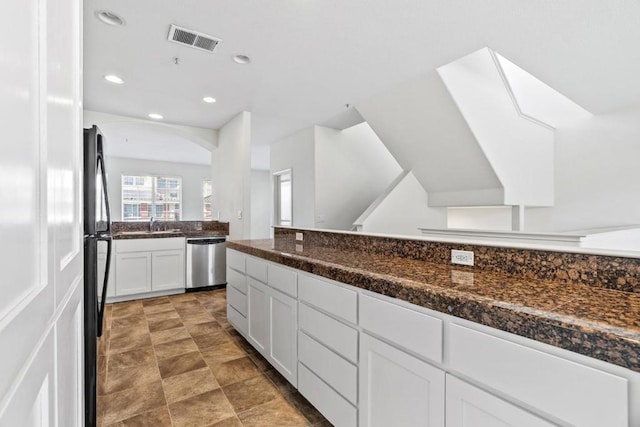 kitchen with dark stone countertops, black refrigerator, stainless steel dishwasher, and white cabinets