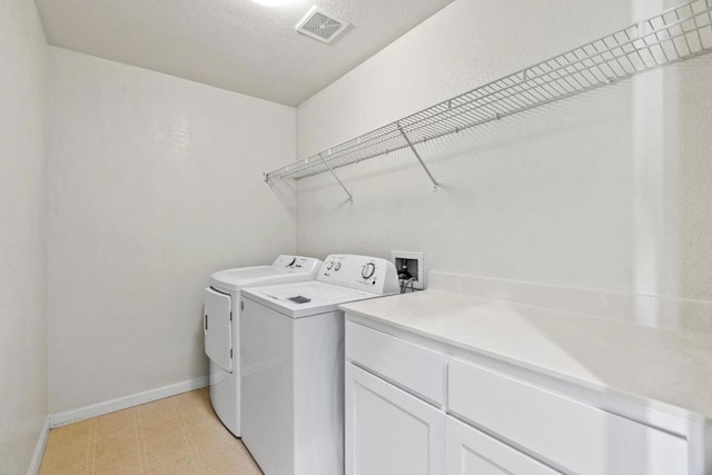 washroom with cabinets, washing machine and dryer, and a textured ceiling