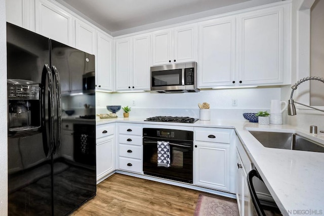 kitchen featuring black appliances, light wood-type flooring, white cabinetry, and sink