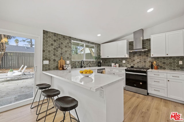 kitchen featuring appliances with stainless steel finishes, a kitchen breakfast bar, white cabinetry, and wall chimney exhaust hood