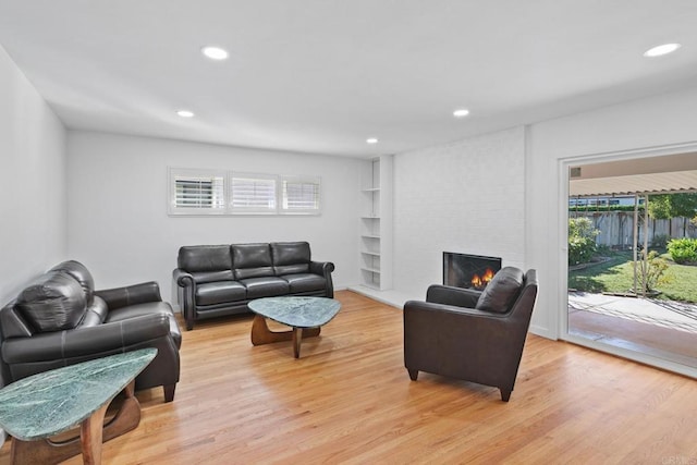 living room with built in shelves, a large fireplace, and light hardwood / wood-style flooring