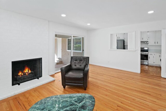 sitting room with a brick fireplace and light wood-type flooring