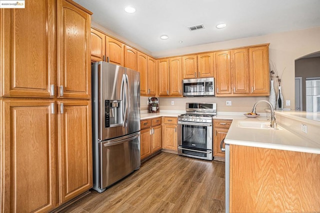 kitchen featuring appliances with stainless steel finishes, dark hardwood / wood-style floors, kitchen peninsula, and sink