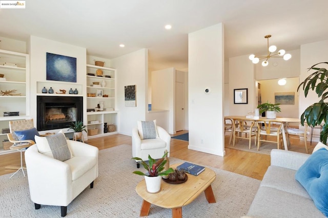 living room with built in shelves, a chandelier, and light hardwood / wood-style floors