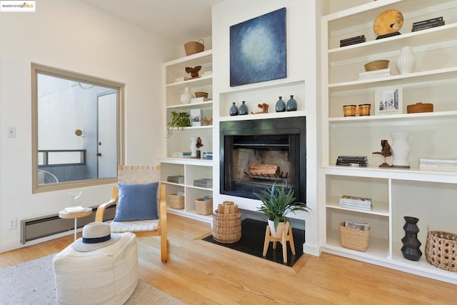 living area featuring hardwood / wood-style floors, built in features, a fireplace, and a baseboard heating unit