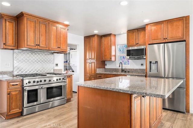 kitchen featuring sink, light stone counters, light hardwood / wood-style flooring, a kitchen island, and appliances with stainless steel finishes