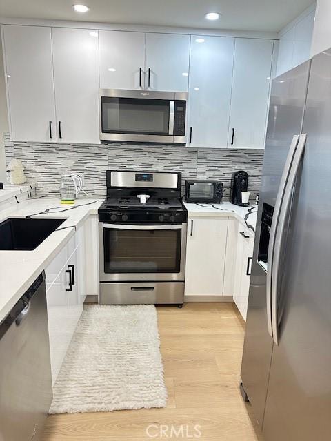 kitchen with stainless steel appliances, backsplash, white cabinets, and light hardwood / wood-style floors