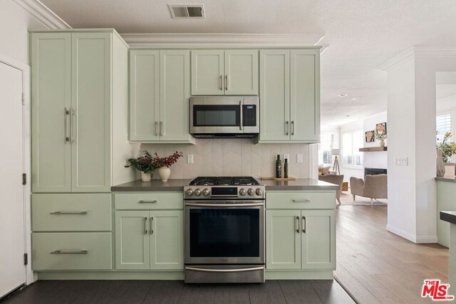 kitchen featuring appliances with stainless steel finishes, ornamental molding, tasteful backsplash, and green cabinets