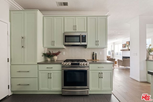 kitchen with green cabinets, appliances with stainless steel finishes, crown molding, and backsplash