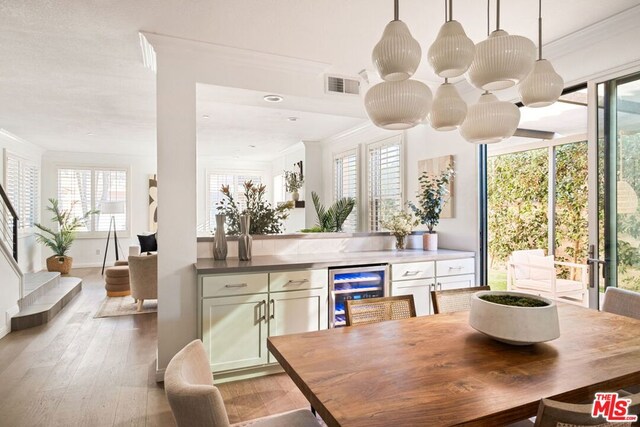 dining room featuring a healthy amount of sunlight, light hardwood / wood-style floors, crown molding, and wine cooler