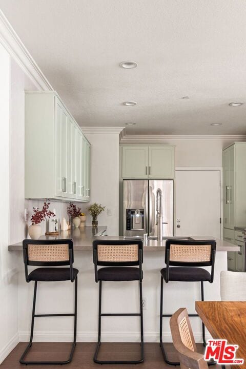 kitchen featuring stainless steel refrigerator with ice dispenser, a breakfast bar area, kitchen peninsula, and green cabinetry