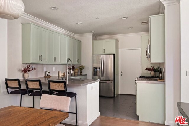 kitchen with stainless steel appliances, green cabinetry, sink, ornamental molding, and kitchen peninsula