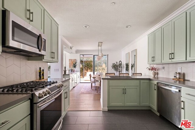 kitchen featuring hanging light fixtures, sink, green cabinetry, appliances with stainless steel finishes, and stainless steel counters