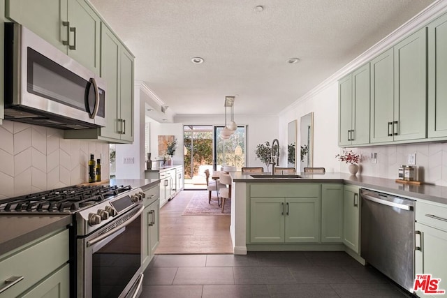 kitchen featuring stainless steel counters, stainless steel appliances, sink, hanging light fixtures, and green cabinets