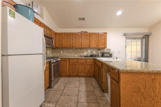 kitchen with light stone countertops, appliances with stainless steel finishes, decorative backsplash, sink, and kitchen peninsula