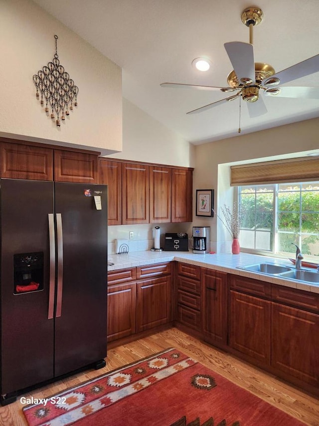 kitchen with lofted ceiling, sink, ceiling fan, black fridge with ice dispenser, and light hardwood / wood-style floors