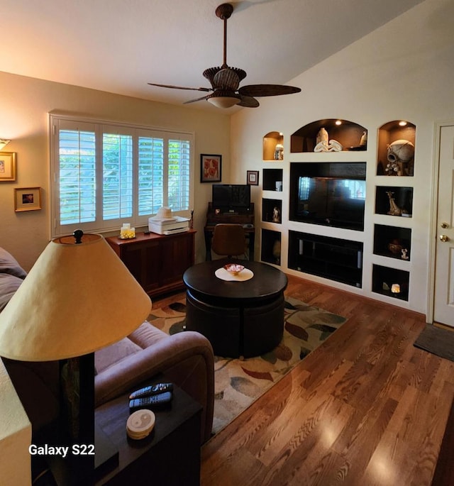 living room with built in shelves, wood-type flooring, and ceiling fan