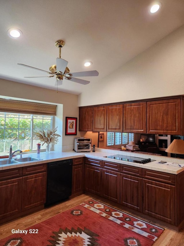 kitchen with lofted ceiling, sink, light wood-type flooring, kitchen peninsula, and black appliances