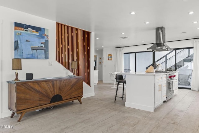 kitchen with high end stainless steel range, white cabinetry, a center island, a kitchen breakfast bar, and island exhaust hood