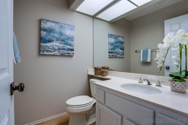 bathroom with toilet, a skylight, hardwood / wood-style floors, and vanity