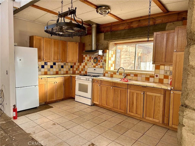 kitchen with sink, decorative light fixtures, wall chimney exhaust hood, white appliances, and backsplash