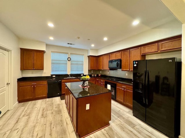 kitchen with a kitchen island, dark stone countertops, black appliances, and light hardwood / wood-style flooring