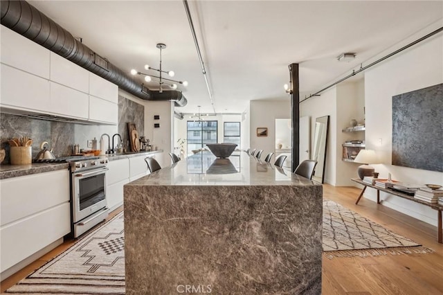 kitchen featuring a kitchen island, white cabinets, stainless steel range with gas stovetop, and hanging light fixtures