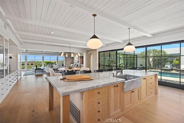 kitchen featuring light stone countertops, a center island with sink, pendant lighting, and light brown cabinets