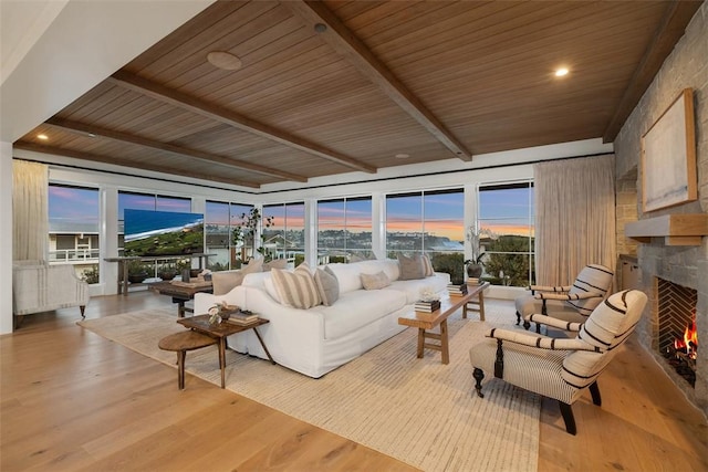 living room featuring beamed ceiling, a fireplace, light hardwood / wood-style flooring, and wooden ceiling