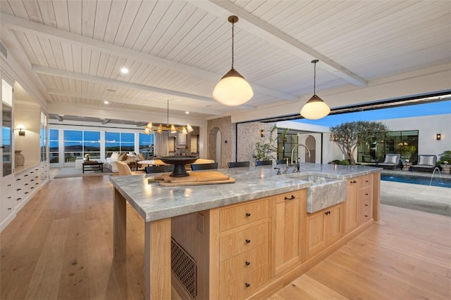 kitchen featuring light hardwood / wood-style floors, hanging light fixtures, a large island with sink, light stone countertops, and light brown cabinets