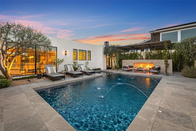 pool at dusk featuring pool water feature, an outdoor fire pit, and a patio area