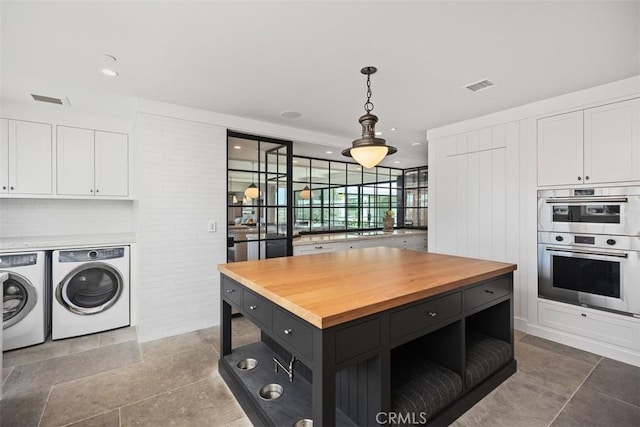 kitchen with washer and dryer, a center island, double oven, pendant lighting, and white cabinetry