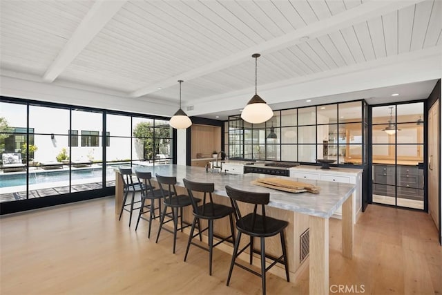 kitchen with light hardwood / wood-style flooring, hanging light fixtures, a kitchen bar, a large island, and beam ceiling