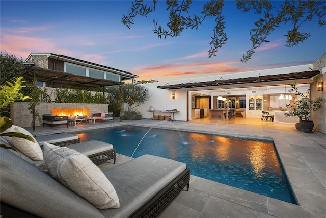 pool at dusk featuring an outdoor fire pit, a patio, pool water feature, and exterior bar