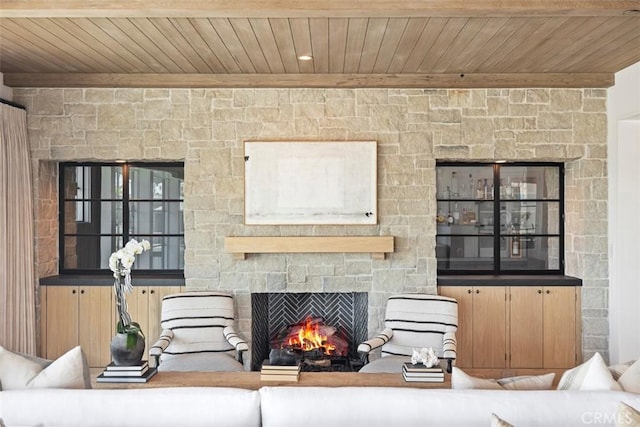 living room featuring beam ceiling, wood ceiling, and a stone fireplace