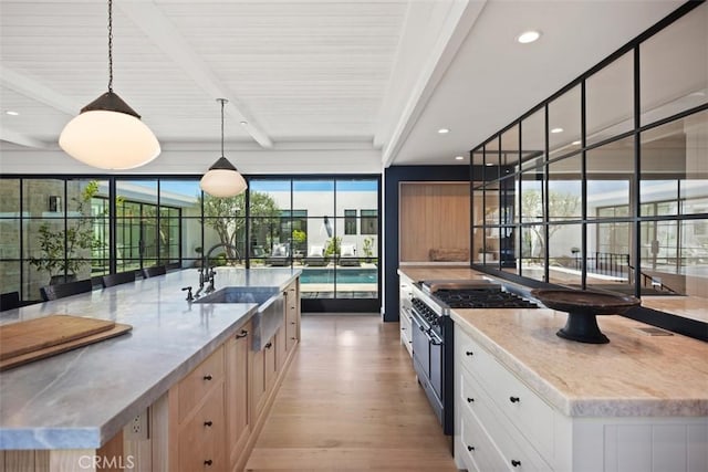 kitchen with a kitchen island with sink, beam ceiling, white cabinets, decorative light fixtures, and sink