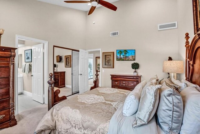 carpeted bedroom with ceiling fan, ensuite bathroom, a closet, and a towering ceiling