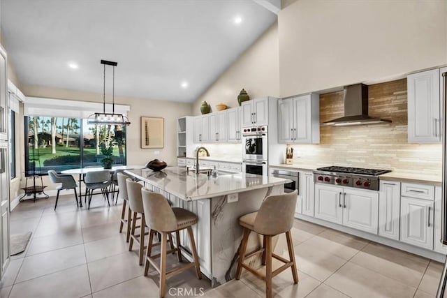 kitchen with wall chimney exhaust hood, tasteful backsplash, pendant lighting, a kitchen island with sink, and appliances with stainless steel finishes