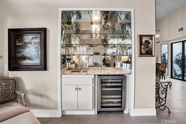 bar with beverage cooler, tile patterned flooring, light stone countertops, sink, and white cabinetry